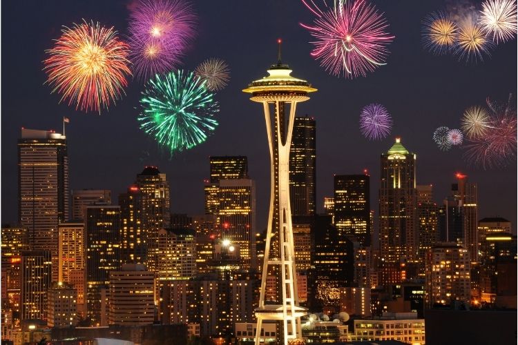 Seattle Space needle with fireworks behind it and night view of city.