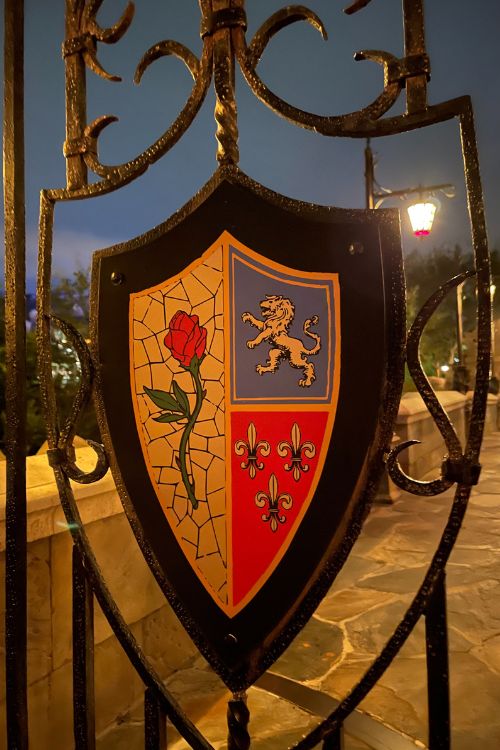 Gate with enchanted rose, lion emblem, and royal arms designs Outside Beast's enchanted Castle