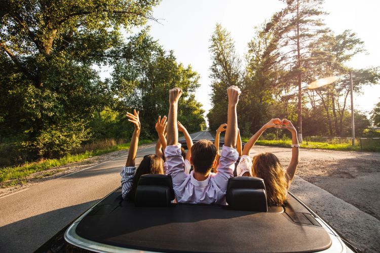 Adults with hands in the air of a convertible during a warm summer day.