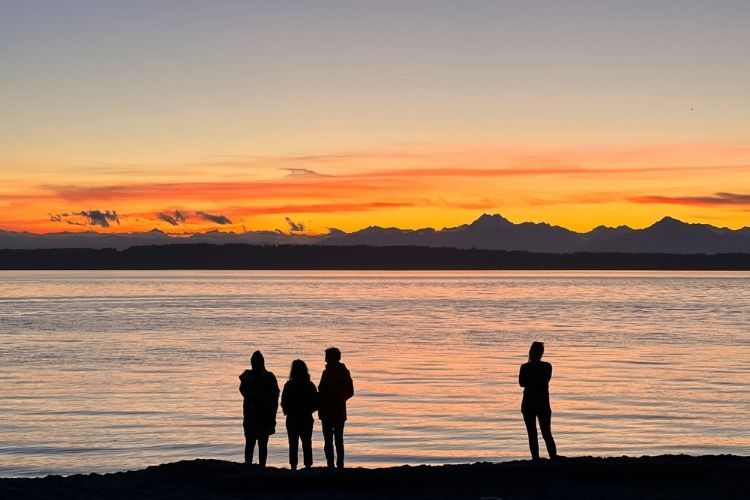 4 people standing watching the sunset at a shore