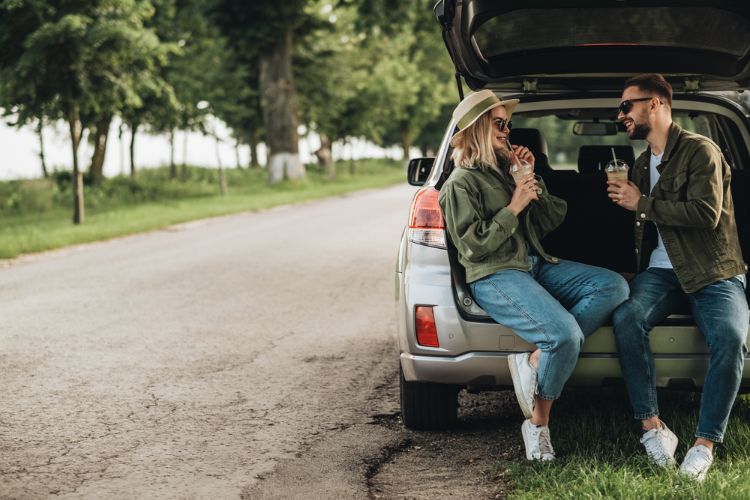 couple sitting in back of car drinking their road trip drinks