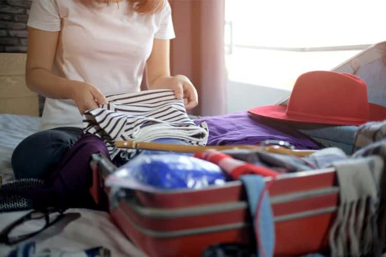 girl packing her weekend travel bag with clothes, and red hat